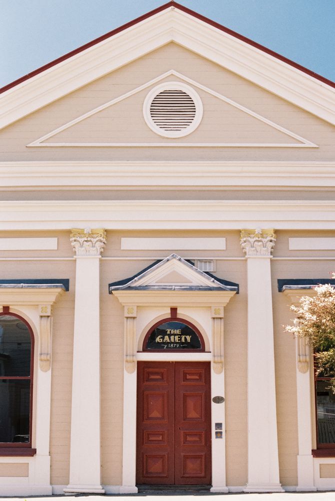 A close up of a cream coloured historical building, centred in frame. A red door sits in the middle and above it is text reading “The Gaiety 1879”.
