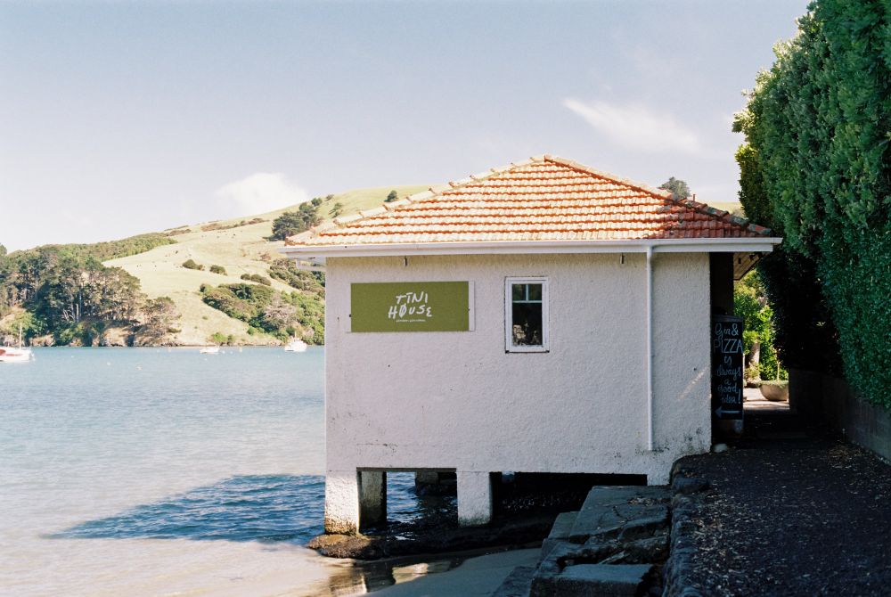 A photo of a small white hut with an orange roof on the edge of a body of water.