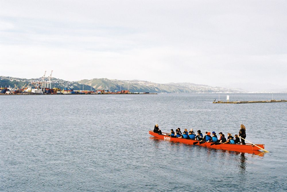 A photo of a long red canoe being rowed out over a bay