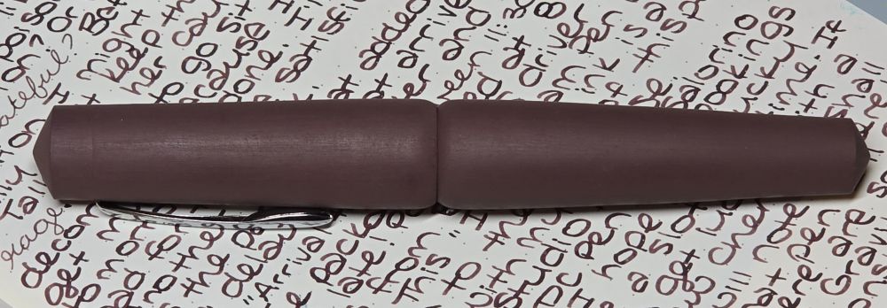A fountain pen rests on a page that is covered in writing. 
The writing was made by the pen in the photo.
The pen is a deep brown/maroon and so is the writing. 