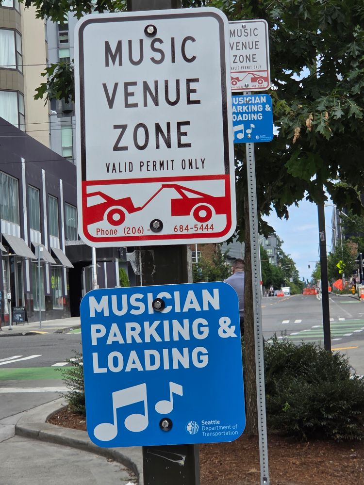 Street sign says "Music Venue Zone (valid permit only)" and includes a red towaway icon, plus a sign in blue below reading "Musician Parking and Loading" plus a pair of eighth notes and a freestanding eighth note. 