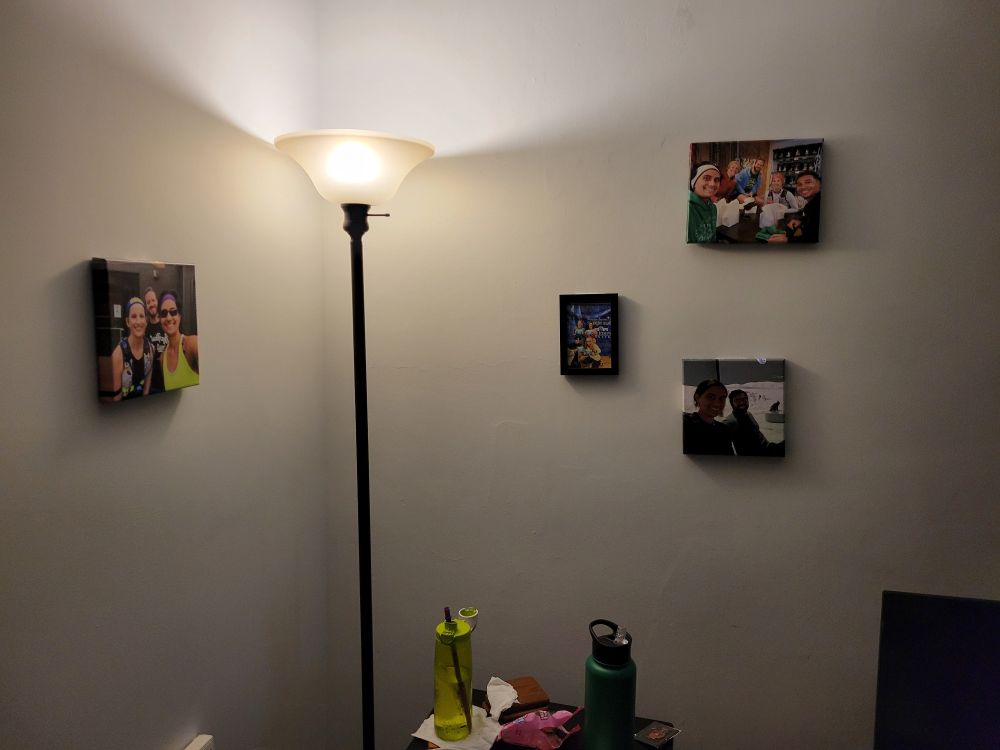 A mix of photos printed on canvasses and photos in black frames hanging on a white wall behind a TV, side table, and floor lamp