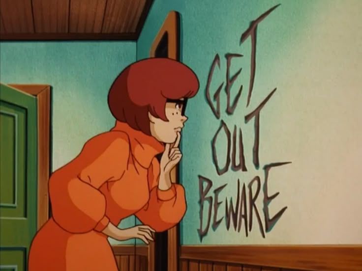 velma (scooby doo) is staring at the wall pensively from a few inches away. carved into the wall in huge letters are the words “GET OUT BEWARE”