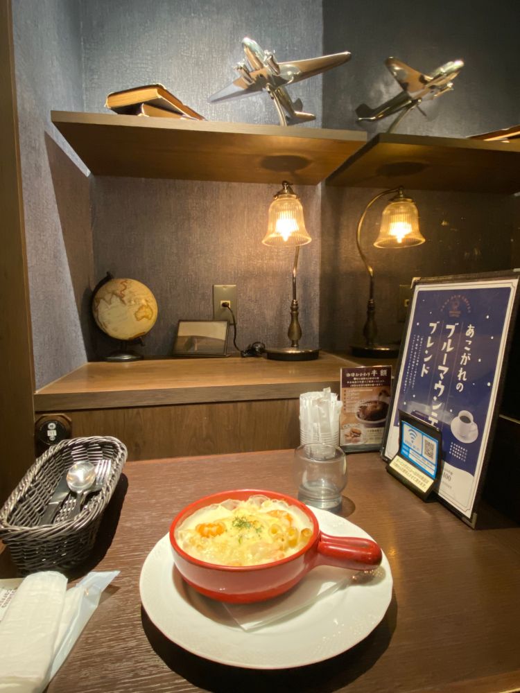 星乃珈琲店　シーフードグラタンと、テーブル前に棚(1段目に地球儀、ランプ　2段目に濃青のハードカバーの本と銀の飛行機が置いてある)