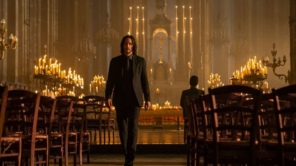 Scene from John Wick 4 with John walking out of a church with dozens of candles behind him. 