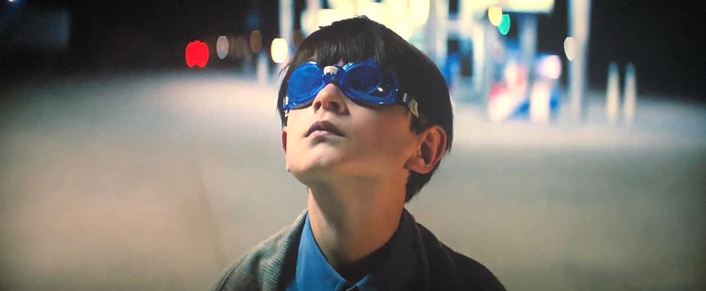 In medium close-up in the foreground of a gas station, blue goggled Alton Meyer (Jaeden Martell), a supernaturally gifted 8-year-old, looks to the night sky.