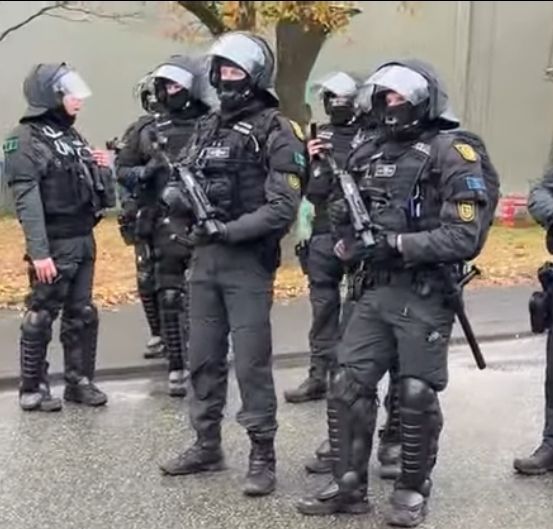 Zu sehen ist eine Gruppe von 8 Polizist*innen, von denen zwei mit Waffen für Gummigeschosse ausgestattet sind.