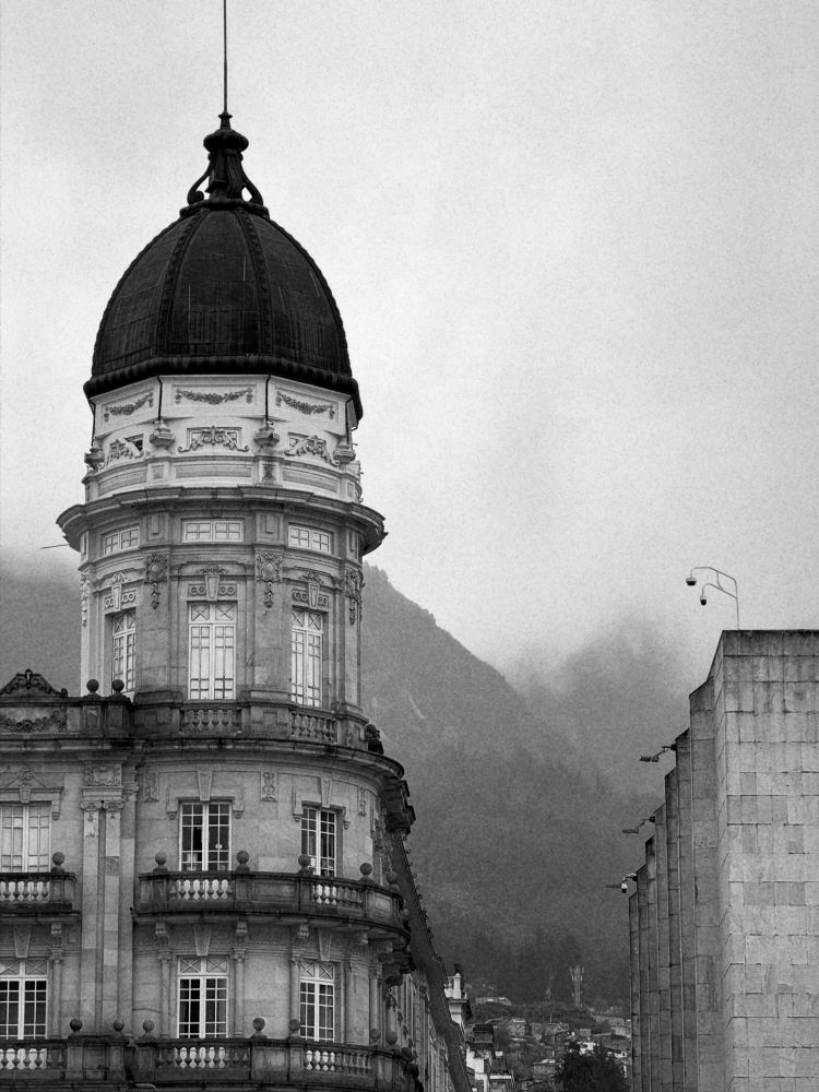 A black and white photo of Colegio Mayor de San Bartolomé with mountains rising into fog in the background.