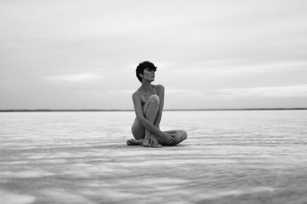 Black and white photo of model Roarie yum posing implied nude on a treeless horizon.
