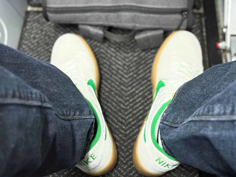 Photo of white and green Nike shoes and a backpack tucked under an airplane seat.