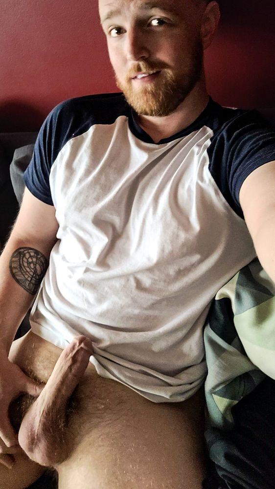 Bearded person in a blue and white shirt with no pants and a hard penis 