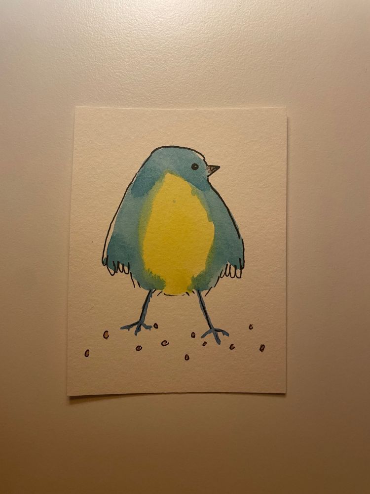 A little bird standing with long legs. The centre of it is a lemon yellow oval with a nice light blue surrounding it. The blue forms wings and a little bump on the top to form the head shape. The bird is facing the right and you can see one eye and it’s beak. There are little circles on the ground to indicate that it’s standing on dirt