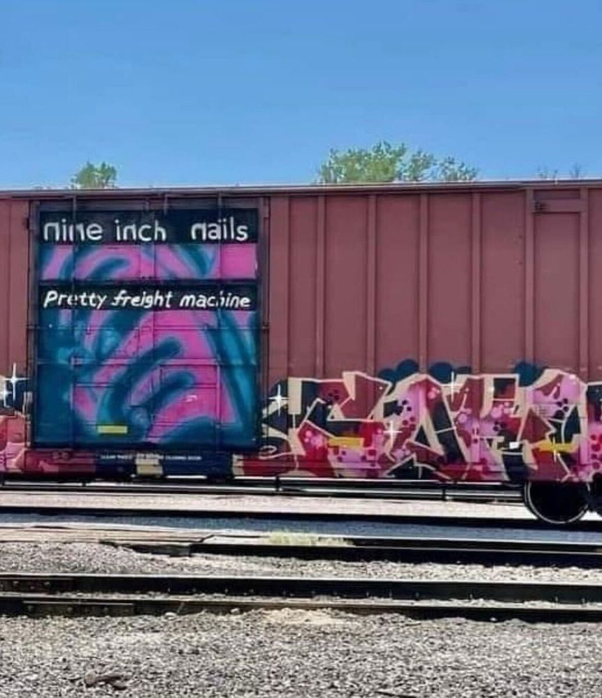 A train freight car with graffiti in the style of the cover art for Nine Inch Nail's "Pretty Hate Machine" except the text says "Pretty Freight Machine".