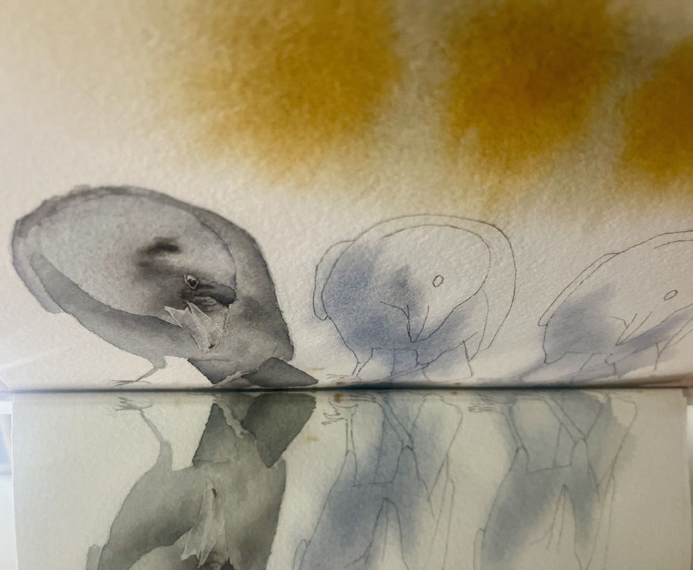 A close-up of a watercolor painting featuring abstract representations of three crows, with soft, muted colors and reflection effects. The background includes warm yellow tones.