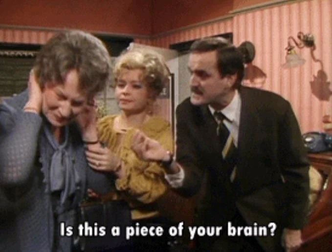 Basil Fawlty (John Cleese) offers a scrap of paper he’s found on the floor to stubborn, hard-of-hearing hotel guest Mrs Alice Richards, shouting “Is this a piece of your brain?”