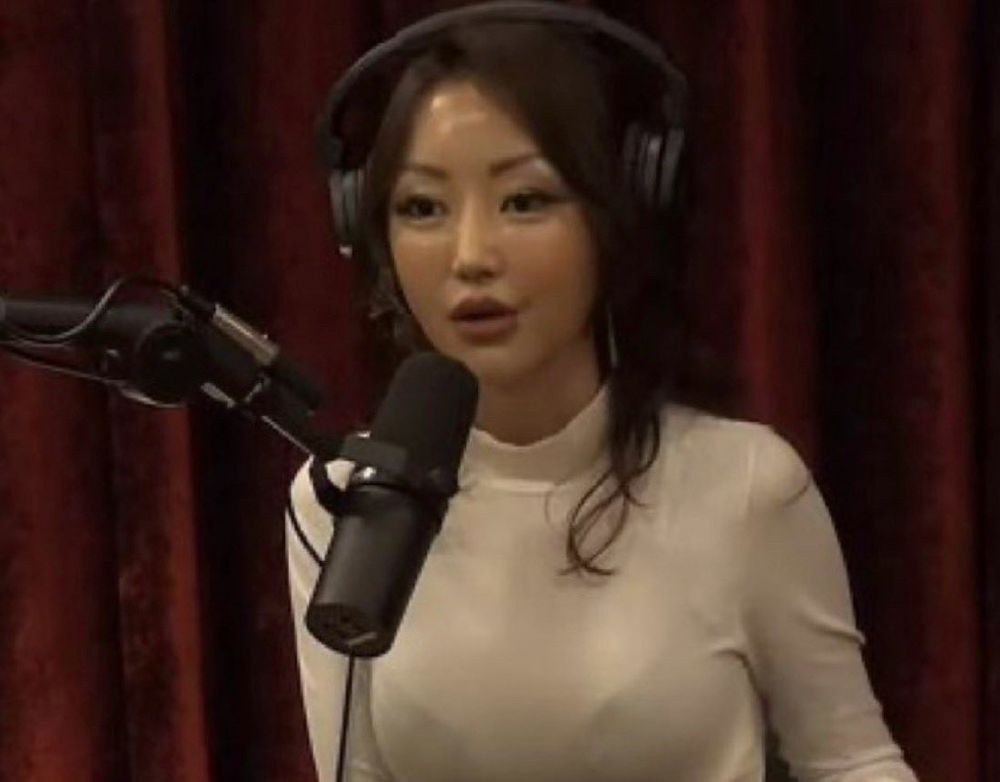 North Korean defector Yeonmi Park, a young woman with long black hair in a white mock turtleneck, wears headphones and speaks into a large podcast microphone 
