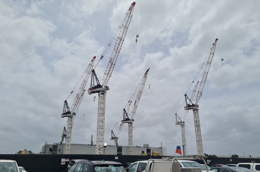 Seven cranes towering over a construction site containing a half built data centre 