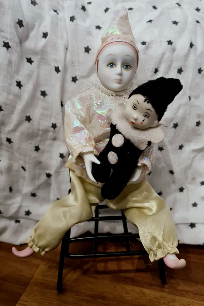 Two decorative clown figurines. One appears to be a crying baby clown and is being held by the adult clown who is sitting
