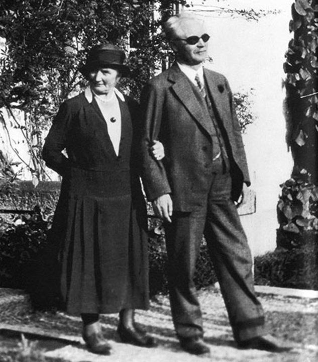 A black-and-white photo of Elma and Gustaf Dalen. He's wearing a three-piece suit with a watch chain, she's got a 1930s hat and a dress with a top that resembles a suit jacket and a string of pearls. He's also wearing dark glasses and not looking at the camera, and she holds his arm protectively while looking slightly sceptically at the camera.