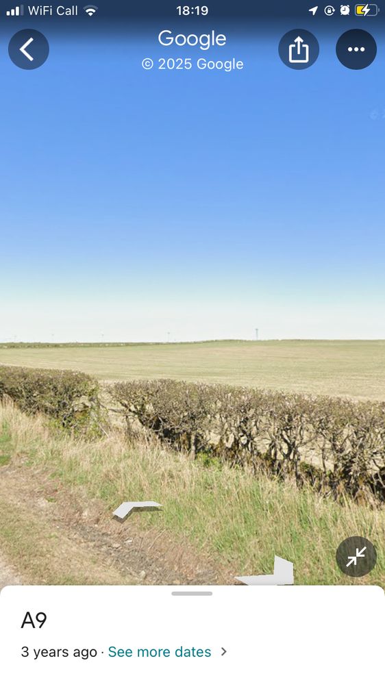 A Google Streetview photo taken from the A9 between Thurso and Georgemas Junction. There’s a winter-bare hedge in the foreground, and the background is flat, empty fields