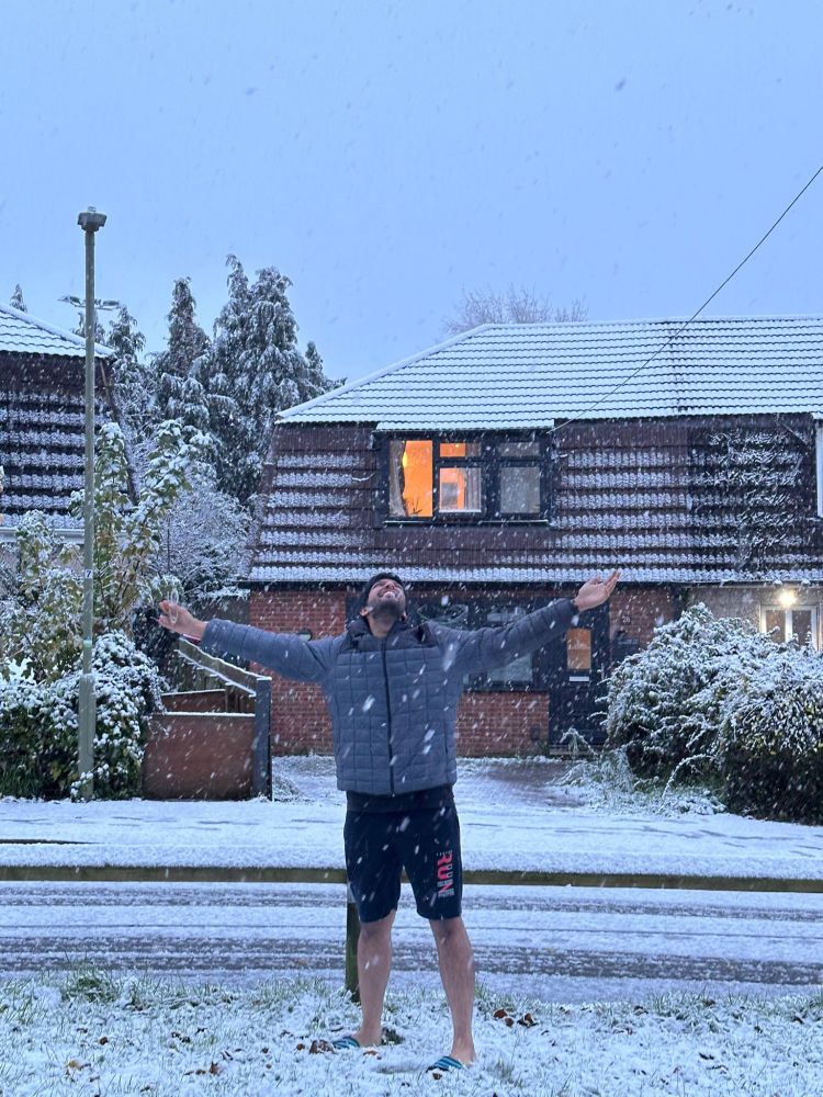 Man extending his arms out, facing the sky to embrace the snow. There is snow everywhere around him