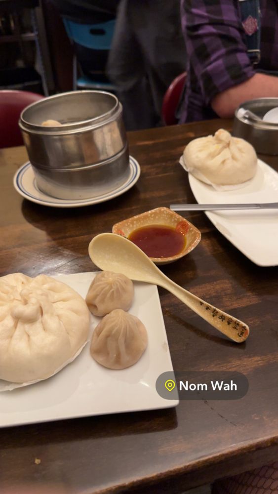 Photo of a dinner table with various dumplings and serving plates. A Snapchat geo tag is in the bottom right corner, which reads “Nom Wah”. 