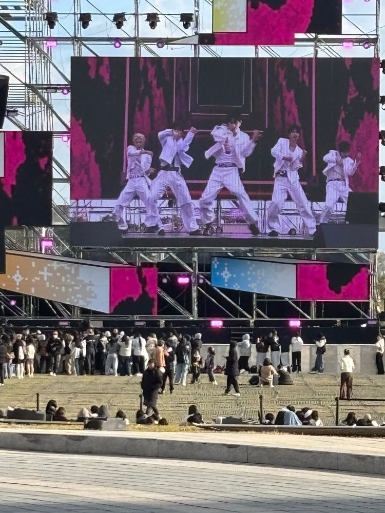 A Korean k-pop band, NOWZ, on the giant screen at an outdoor music festival in Incheon, Korea. 5 of them dressed all in white throw coordinated shapes. 