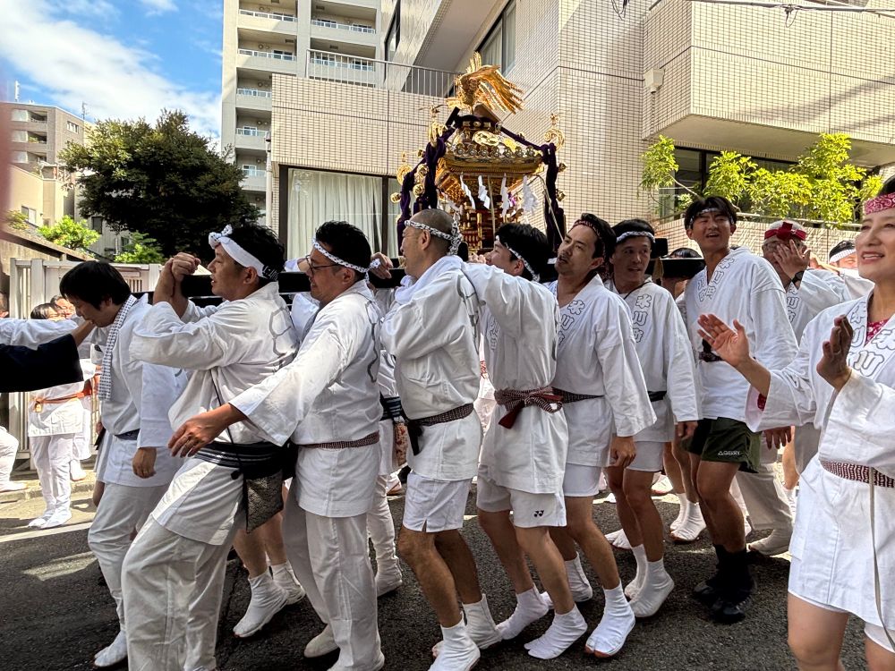 Japanese men carry a portable shrine called a mikoshi at the Akasaka Hikawa festival. The mikoshi is highly decorated and a golden bird with wings unfolded sits atop. 