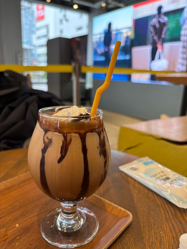 A glass filled with a cafe mocha. Chocolate dribbles down the side and a straw peeks out. 