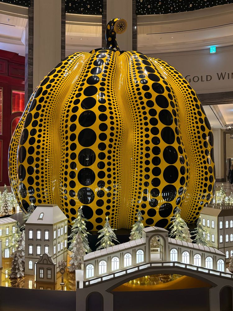 Yayoi Kusama pumpkin. Bigger than a person and covered in dots, sits behind an illuminated Italian minitaure with bridges, buildings, canal & gondola. 