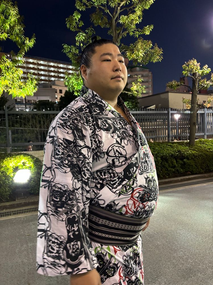 Wakamatoharu is a high ranking sumo. He stands close-by posing for the camera. He wears a cotton yukata robe. He is large & unsmiling, but was generous in his time spent greeting the many waiting fans & signing autographs & taking selfies. Location; Ryokogu Kokugikan. 