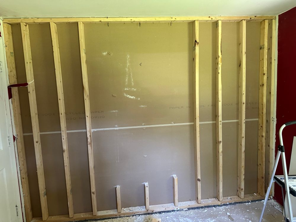 Exposed studs with several cut out, drywall on the other side visible 