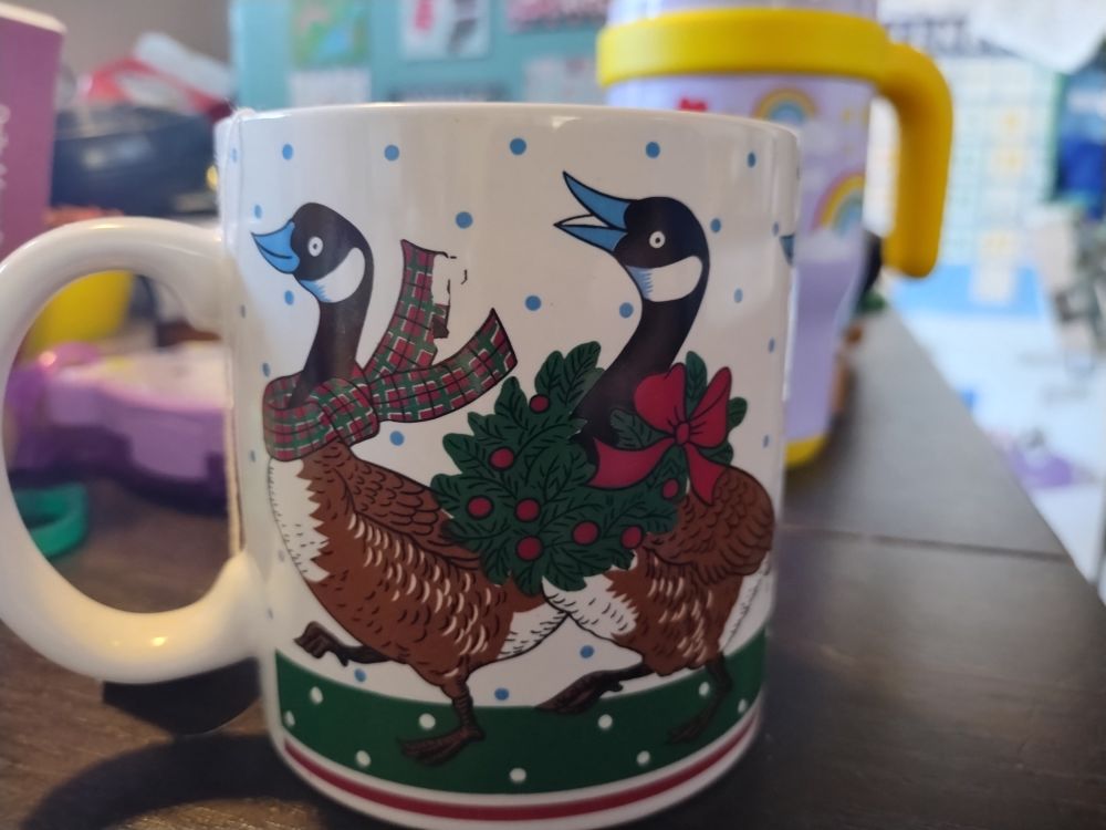 A ceramic mug with Canadian geese on it. Geese are covered in various Christmas paraphernalia - wreaths, bows, etc.