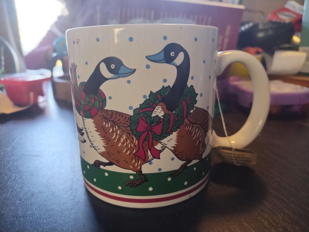 A ceramic mug with Canadian geese on it. Geese are covered in various Christmas paraphernalia - wreaths, bows, etc.
