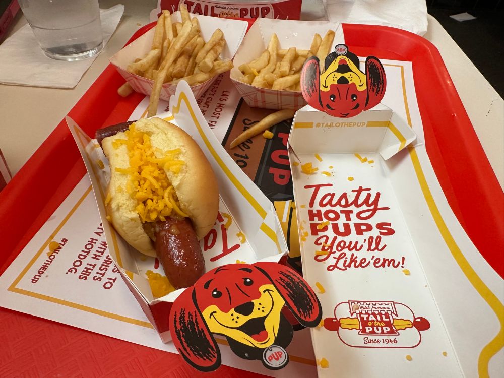 The remains of my second cheese dog, a few servings of French fries and an empty hot dog tray that says on the bottom of it “Tasty hot pups, you’ll like em!” And below that the Tail of the Pup logo. 