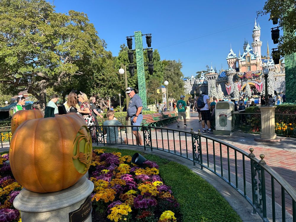 Disneyland resort during Halloween with a pumpkin in the foreground while Sleeping Beauty’s castle has snow on the roof and holiday decorated trees in front of it as part of the filming of the Wonderful World of Disney Magical Holiday Celebration tv special. 