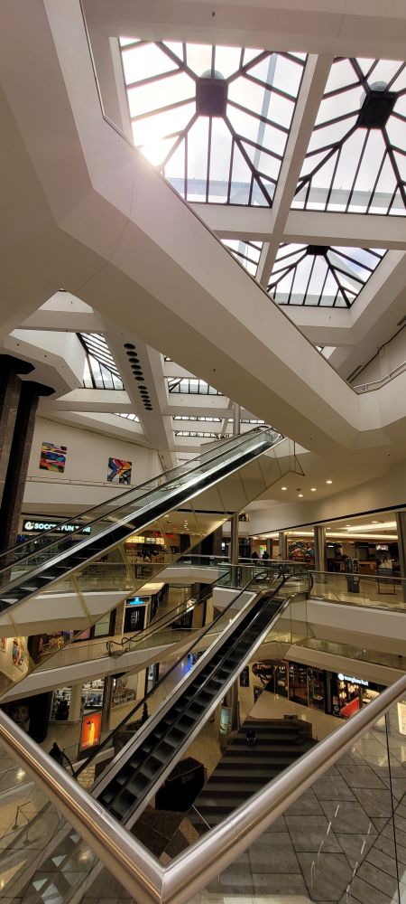 vertical photo of a shopping mall central area with multiple escalators and a skylight. It's a little disorienting