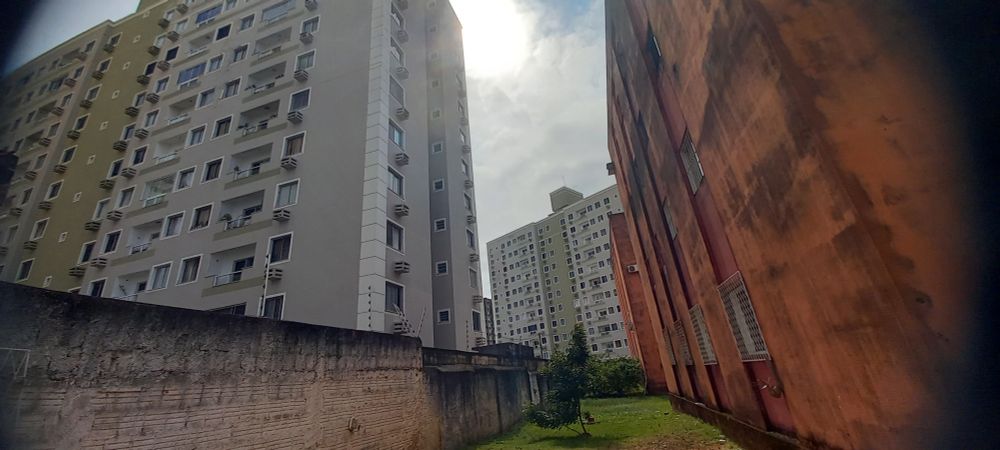 Foto do prédio vizinho, cinza e branco à esquerda. E o prédio onde moro vermelho alaranjado à direita. Entre eles um espaço de 6 metros dividido por um muro de 2 metros de altura. 