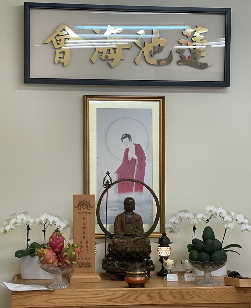And altar with Chinese writing above, a statue of Ksitigharba bodhisattva seated, surrounded by offerings, with a painting of the Buddha on the wall behind