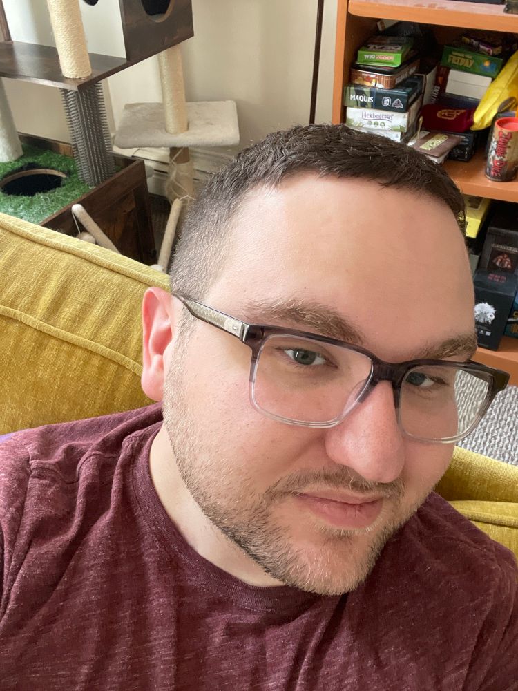 A man with glasses turned to the camera with a half smile in a red t shirt. 