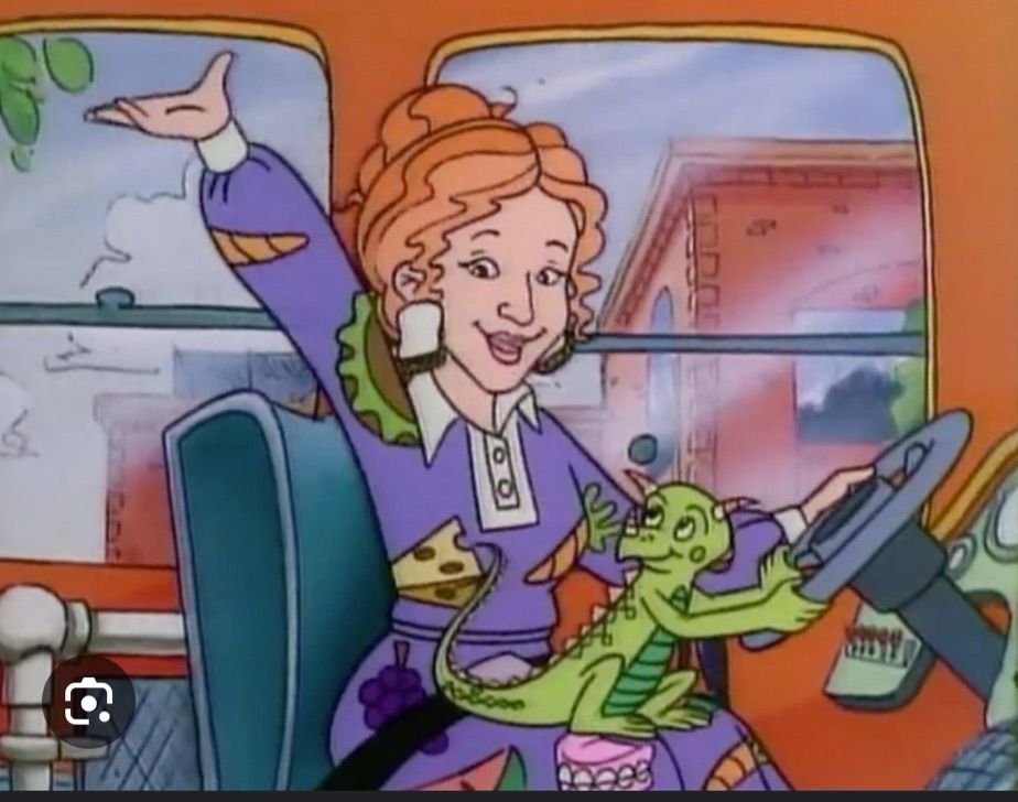 Ms frizzle in her school bus with her hand up and a lizard in her lap
