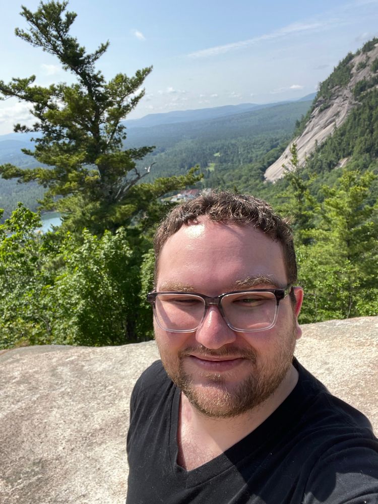 Man smiling at camera with the background of a mountain vista 