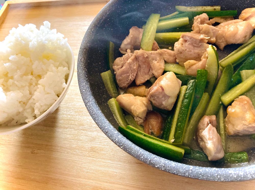 鶏肉ときゅうりの炒め物がフライパンのまま食卓に乗っている写真。左には白いごはん。きゅうりは拍子木切りのようなサイズ、鶏肉は焼き鳥くらいの一口サイズ。