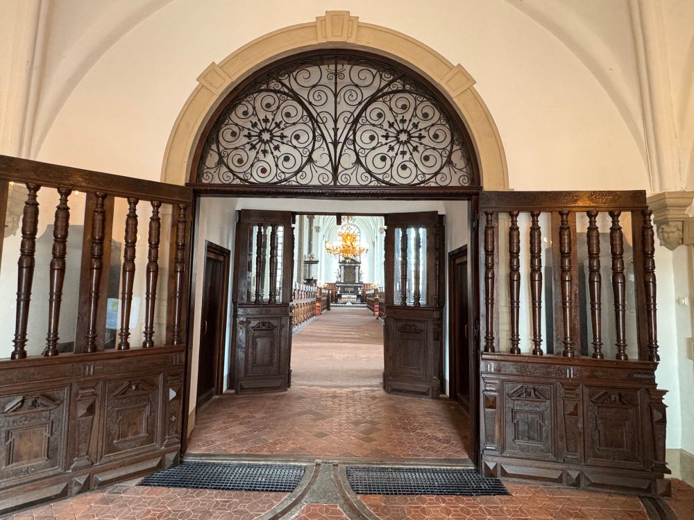 Oude houten deuren staan open bij de ingang van een oude kerk. Mooi glaswerk er boven.