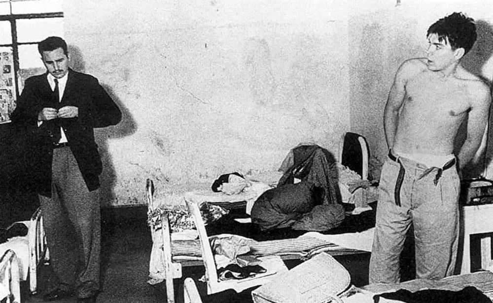 Photo en noir et blanc d'une cellule pénitentiaire. A gauche, fidel castro termine de reboutonner son veston. A droite, ernesto guevara torse nu renfile son pantalon en regardant fixement castro. 