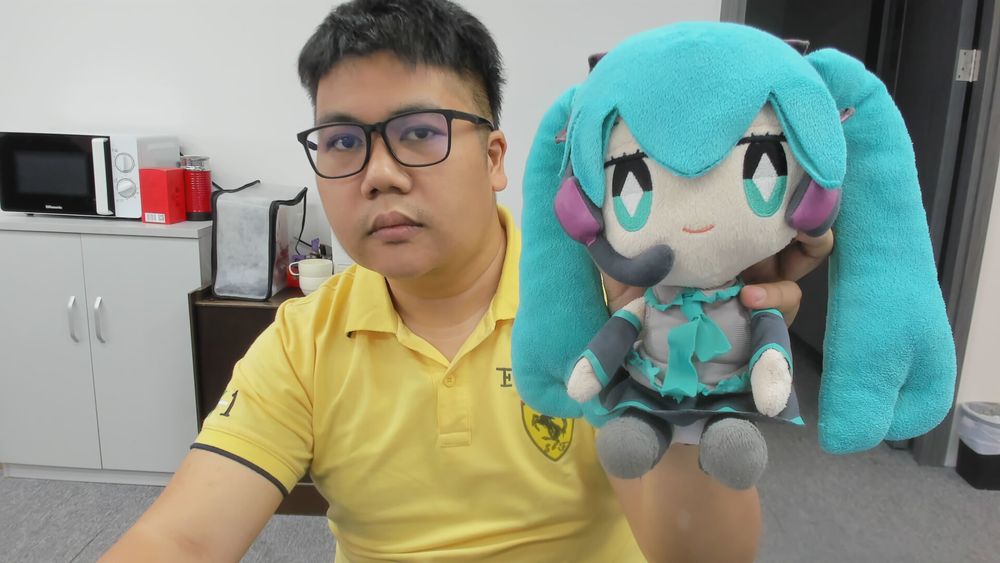 Me with glasses and a yellow collared shirt holding a Miku Hatsune doll