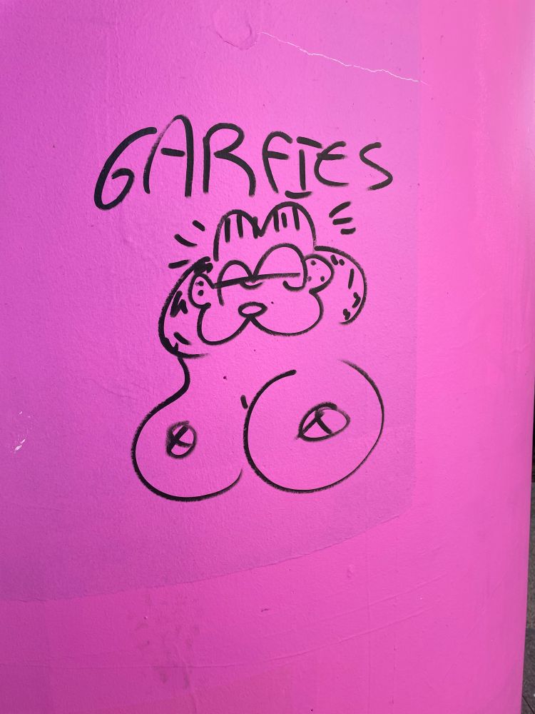 Against a bright pink background, an ink tag of Garfield with big ole titties. Above is written “GARFIES”