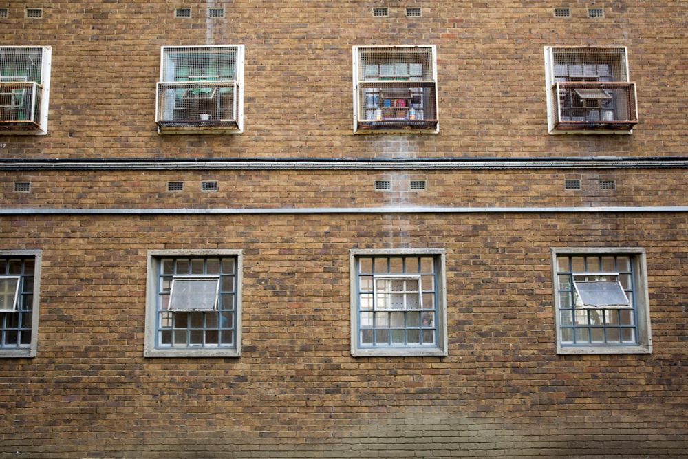 Exterior view of a houseblock in Coldingley prison. Eight barred windows, arranged in two rows of four, set in a brown brick wall.