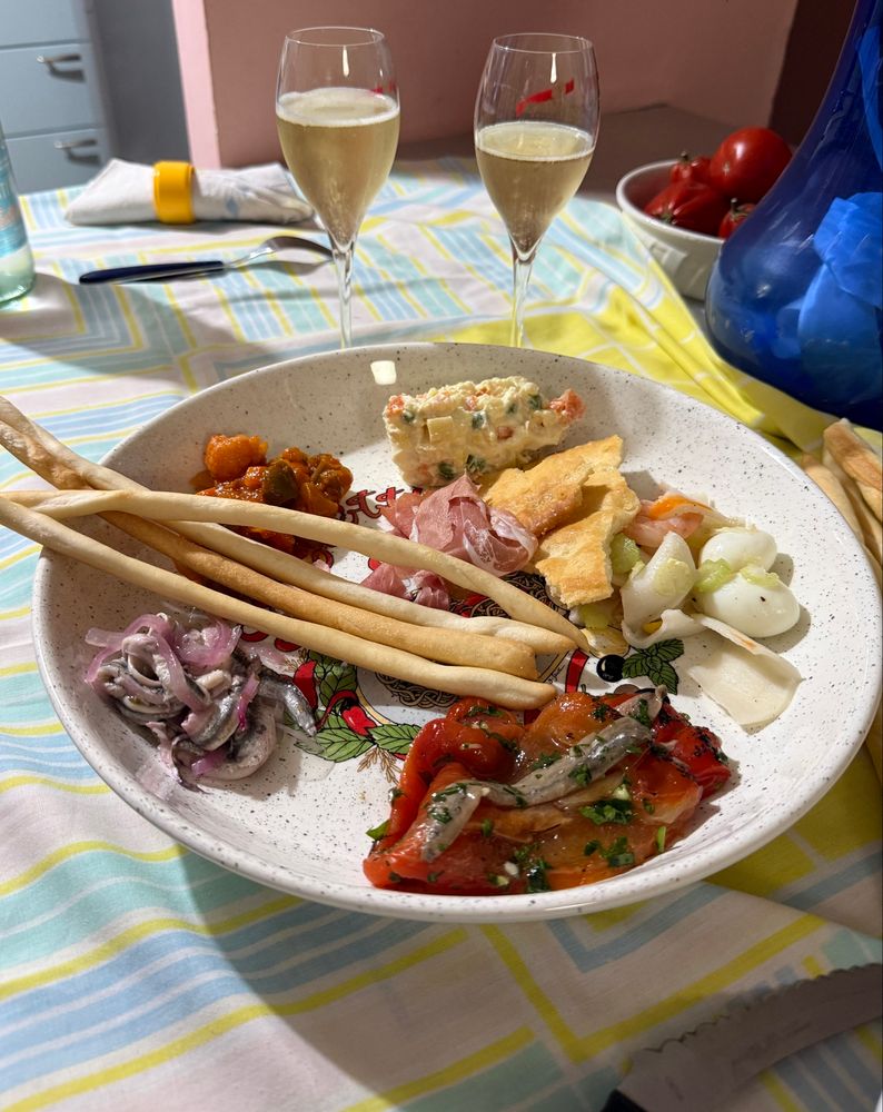 Un piatto con peperoni, alici marinate, grissini, antipasto piemontese, insalata di mare, insalata russa e focaccia secca. Nei bicchieri : Alta Langa