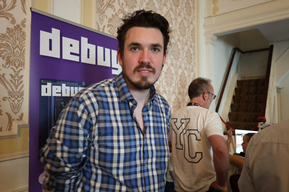 Debug games editor Nick Crocker standing in front of a Debug banner at the Brilliant Indie Showcase in Brighton
